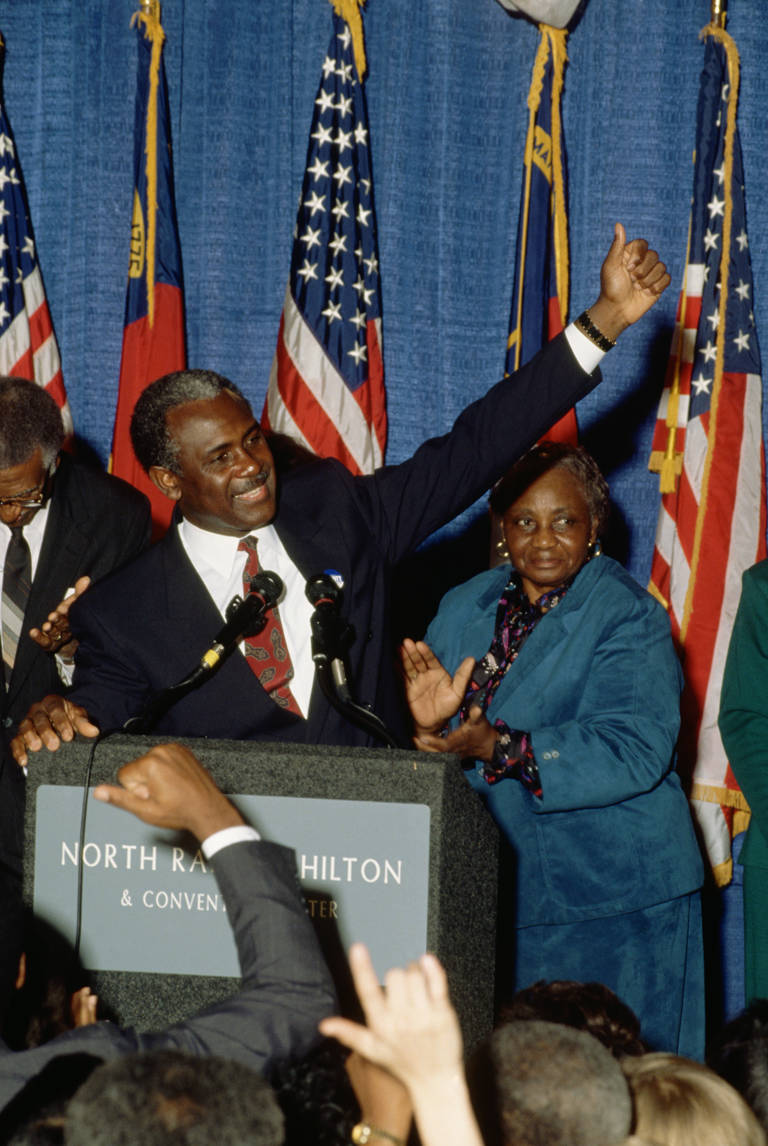 Color photo of North Carolina senatorial candidate Harvey Gantt speaking to supporters on election night in 1990, standing at a podium with his arm raised.