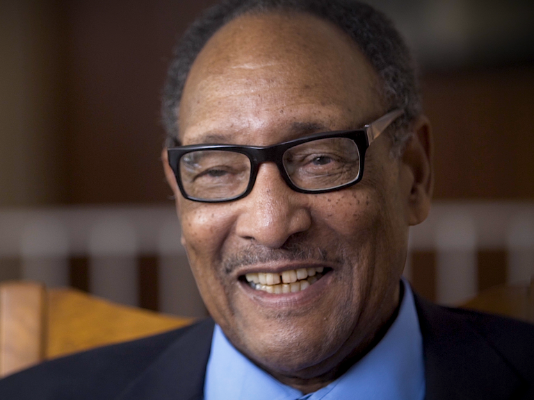 Color photo of Bill Robinson, seated indoors and smiling, during his oral history interview.