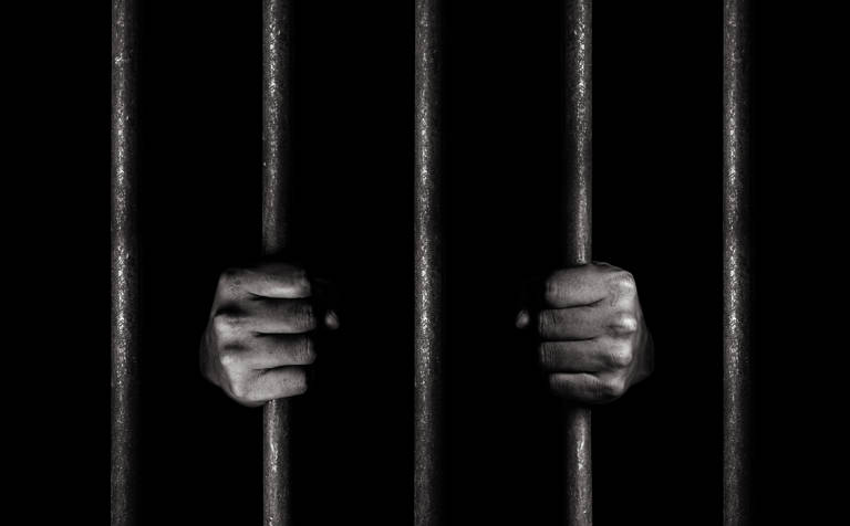 Black-and-white photo of hands gripping jail bars.