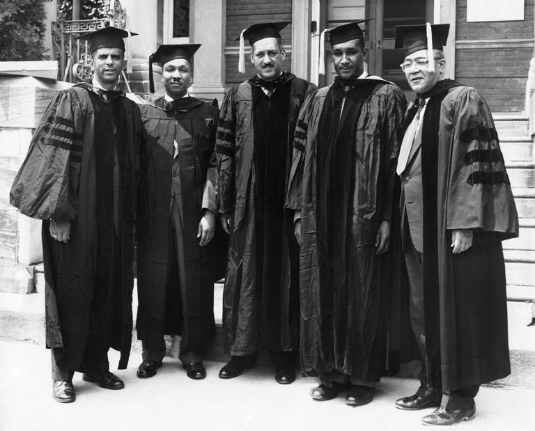 Black-and-white photo of five men wearing academic caps and gowns while standing outside a building. Photographed left to right are Franklin H. Williams, Robert L. Carter, Thurgood Marshall, Clarence M. Mitchell, and Horace Mann Bond.