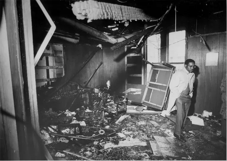 Black-and-white photo of Julius Chambers walking through a dilapidated room filled with detritus.