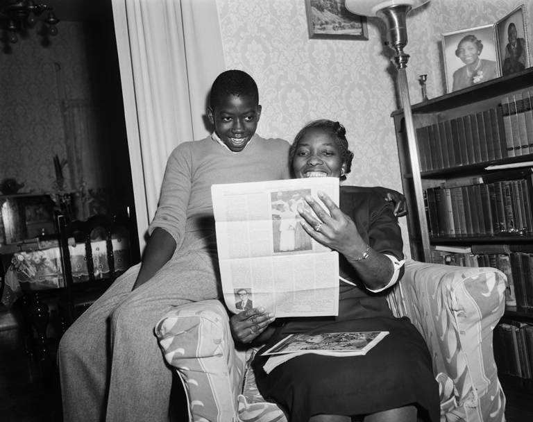 Black-and-white photo of Spottswood Bolling, who was one of the plaintiffs in the May 17, 1954, ruling by the U.S. Supreme Court that racial segregation in public schools is unconstitutional, reading about the court decision in the newspaper the following day with his mother, Sarah Bolling.