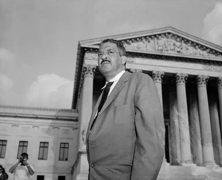 Black-and-white photo of Thurgood Marshall wearing a suit and standing outside of the Supreme Court building.