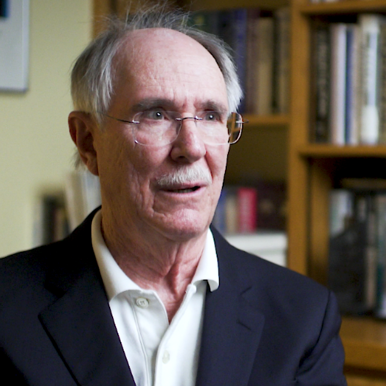 Color photo of Jack Boger, wearing a suit and sitting in front of a bookshelf during his oral history interview.