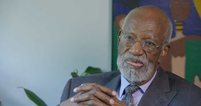 Color photo of James Ferguson, wearing a suit, with his hands clasped in front of him during his oral history interview.