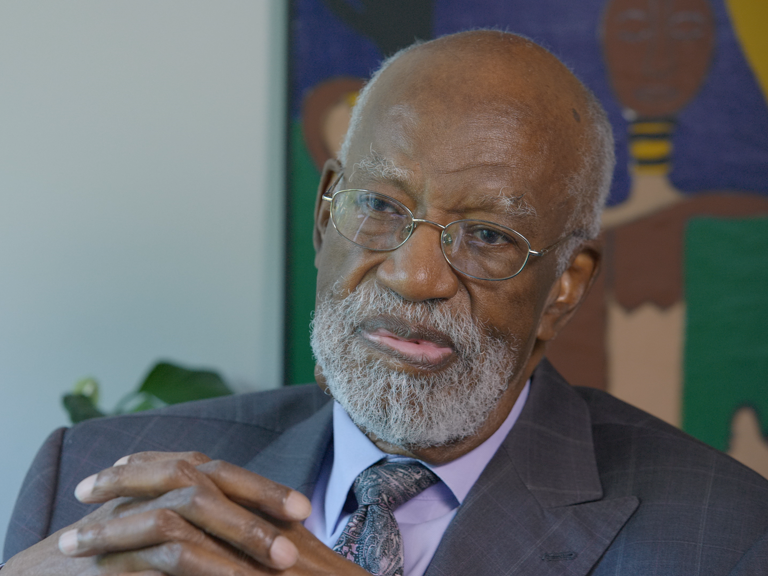 Color photo of James Ferguson, wearing a suit, with his hands clasped in front of him during his oral history interview.