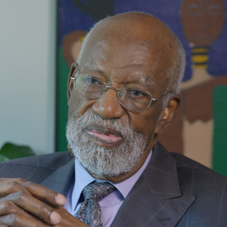 Color photo of James Ferguson, wearing a suit, with his hands clasped in front of him during his oral history interview.