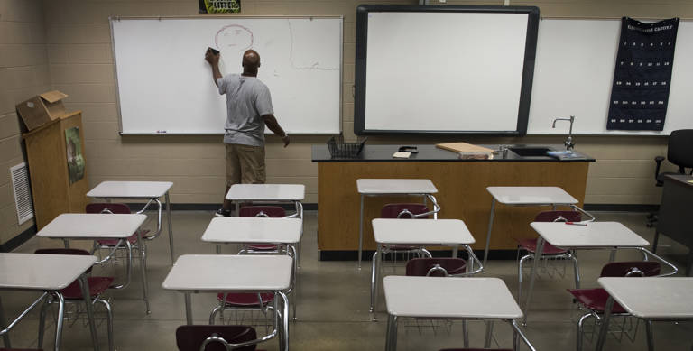 Color photo of a Gardendale High School teacher preparing his classroom on August 4, 2016, before school begins in Gardendale, Alabama. The teacher cleans the whiteboard in front of rows of empty desks.