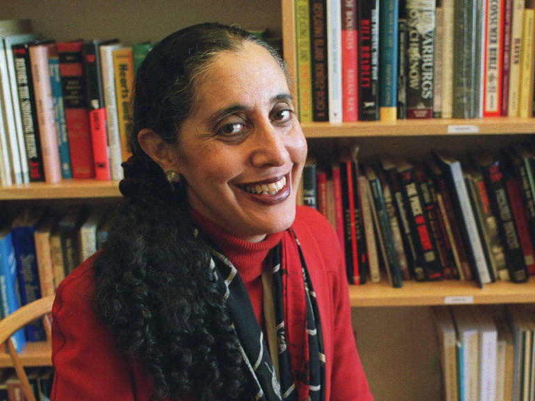 A color photo of Lani Guinier wearing a red shirt while sitting in front of a bookshelf.