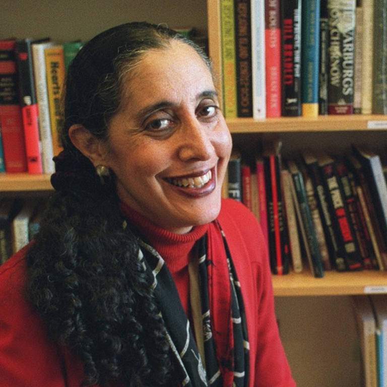 A color photo of Lani Guinier wearing a red shirt while sitting in front of a bookshelf.