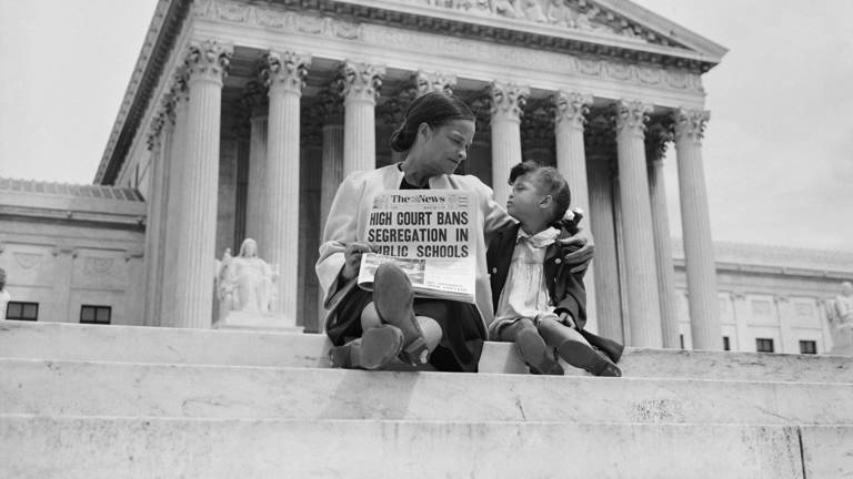 Black-and-white photo of Nettie Hunt and her daughter Nickie sitting on the steps of the U.S. Supreme Court building, as Nettie holds a newspaper with a headline reading, "High Court Bans Segregation in Public Schools."