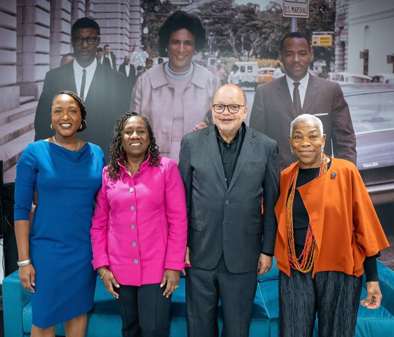 Color photo of (from left to right) Janai Nelson, Sherrilyn Ifill, Ted Shaw, and Elaine Jones standing in front of a color photo of past LDF attorneys.