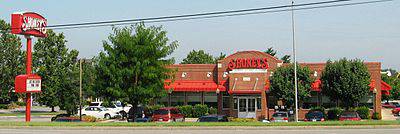 Color photo of the exterior of Shoney's Restaurant, a red brick building with cars parked in the parking lot and a large red and white Shoney's sign.