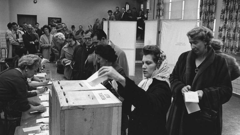 Black-and-white photo of voters at a polling station in Dunn Loring, Virginia, on November 8, 1960, with a white woman placing her ballot in the box in the foreground.