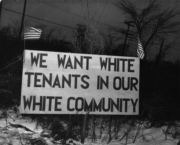 Black-and-white photo of a sign placed across from the Sojourner Truth housing project in Detroit, Michigan, in February 1942, reading, "We want white tenants in our white community."