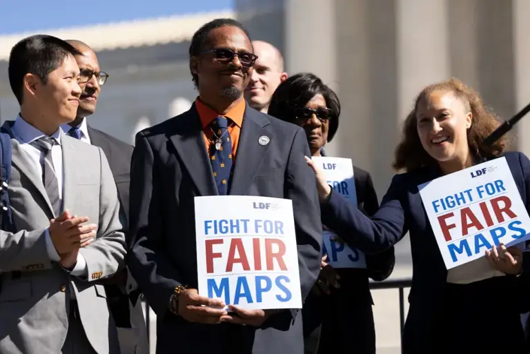 Color photo of plaintiffs Taiwan Scott and South Carolina NAACP President Brenda Murphy standing with LDF Senior Counsel Leah Aden at a press conference after oral arguments in Alexander v. South Carolina State Conference of the NAACP on October 11, 2023. They hold signs stating, "LDF Fight for Fair Maps."