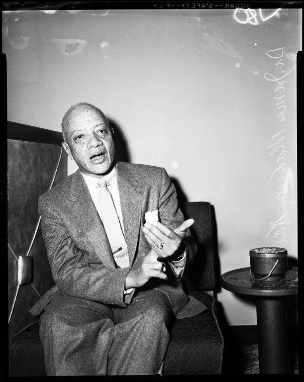 Black-and-white photo of James Nabrit sitting in a chair and talking, with a side table next to him.