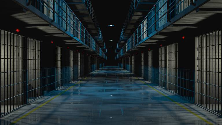 Color photo of the interior of a prison corridor at night, showing cells with lights on.