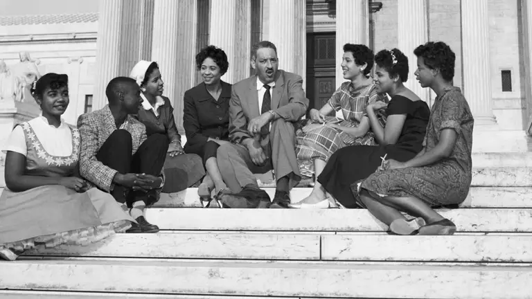 Black-and-white photo of Thurgood Marshall sitting on the steps outside of the Supreme Court building with several members of the Little Rock Nine.