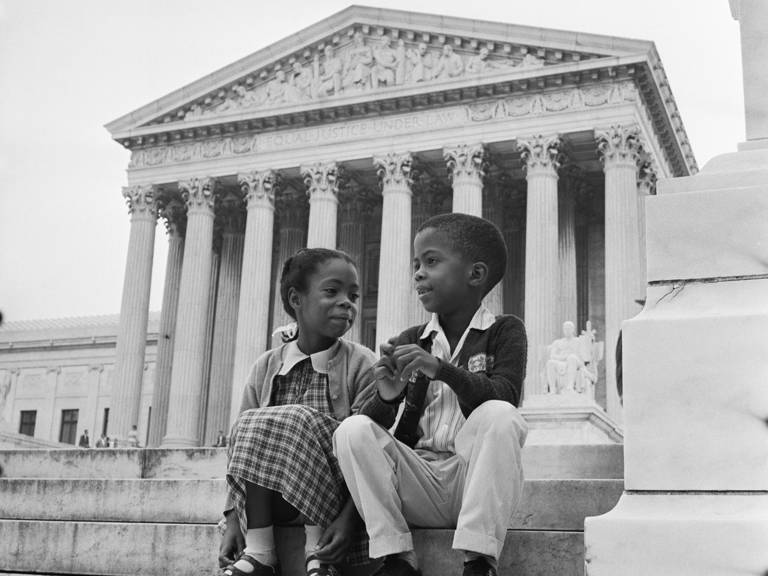 Black-and-white photo of two young Black children sitting on the steps outside the U.S. Supreme Court building during arguments about the integration Little Rock Schools.