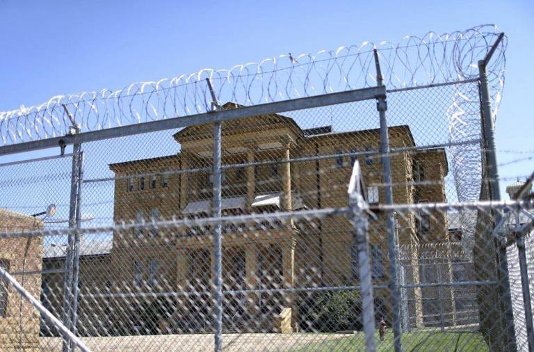 Color photo of Menard Correctional Center, with a fence and barbed wire in the foreground and the facility in the background.