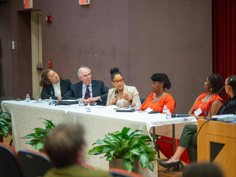 Karla McKanders speaks into a microphone during the panel “History Is a Call to Action: Building the Record and Imagining the Future,” while fellow panelists seated at the table listen.
