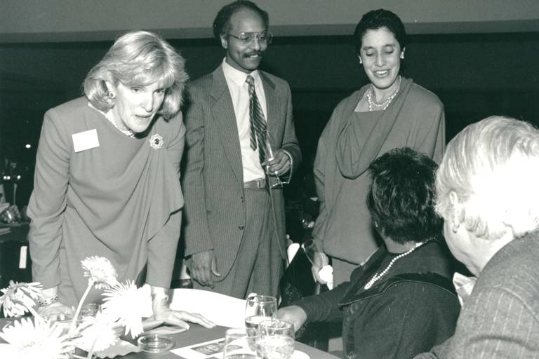 Black-and-white photo of five people speaking, with two sitting at a table and three (including Lani Guinier) standing.