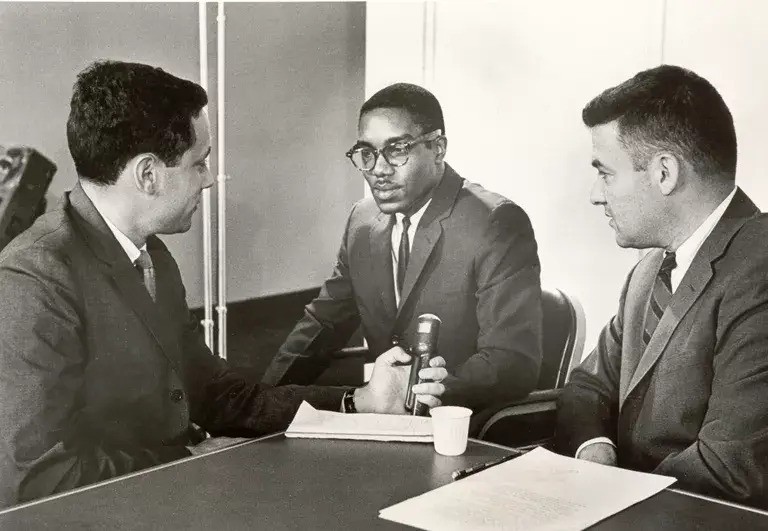 Black-and-white photo of a young Julius Chambers (center) conducting an interview, seated between two other men.