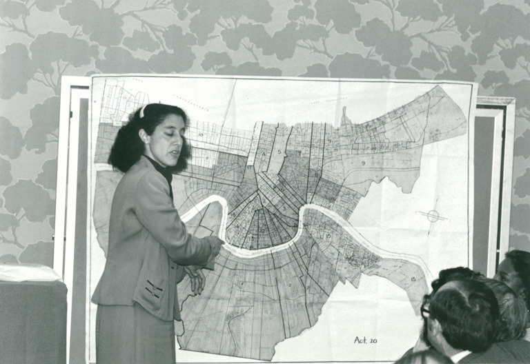 Black-and-white photo of Lani Guinier standing in front of a legislative map and talking to seated people.