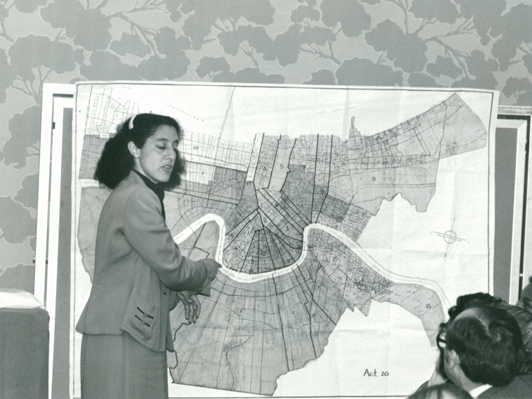 Black-and-white photo of Lani Guinier standing in front of a legislative map and talking to seated people.