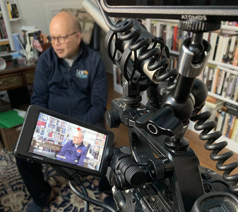 Color photo of Ted Shaw, seated and wearing an LDF sweatshirt, in front of a video camera during his oral history interview.