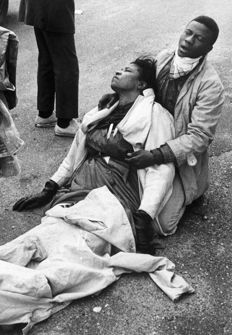 Black-and-white photo of a civil rights marcher holding an unconscious Amelia Boynton Robinson on the ground after mounted police officers attacked marchers in Selma, Alabama, as they were beginning a 50-mile march to Montgomery to protest racial discrimination in voter registration.