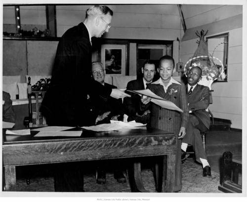 Black-and-white photo of school staff at Phillis Wheatley Elementary School giving a certificate to a young Black student as other adults look on.