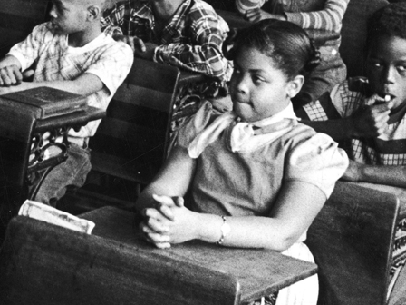 Black-and-white photo of several Black children sitting at their desks in a classroom.